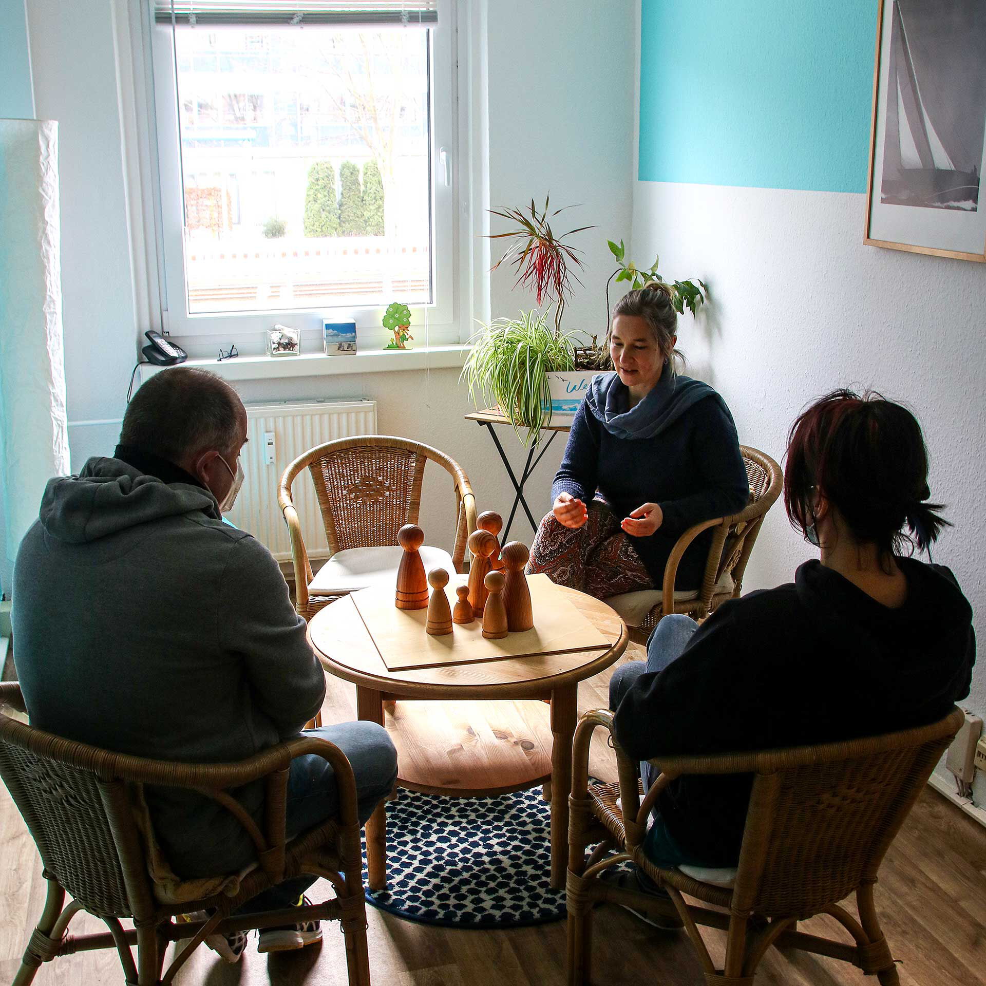 Ein Therapiegespräch von 3 Erwachsenen mit einer Personenaufstellung in Form von Holzfiguren.