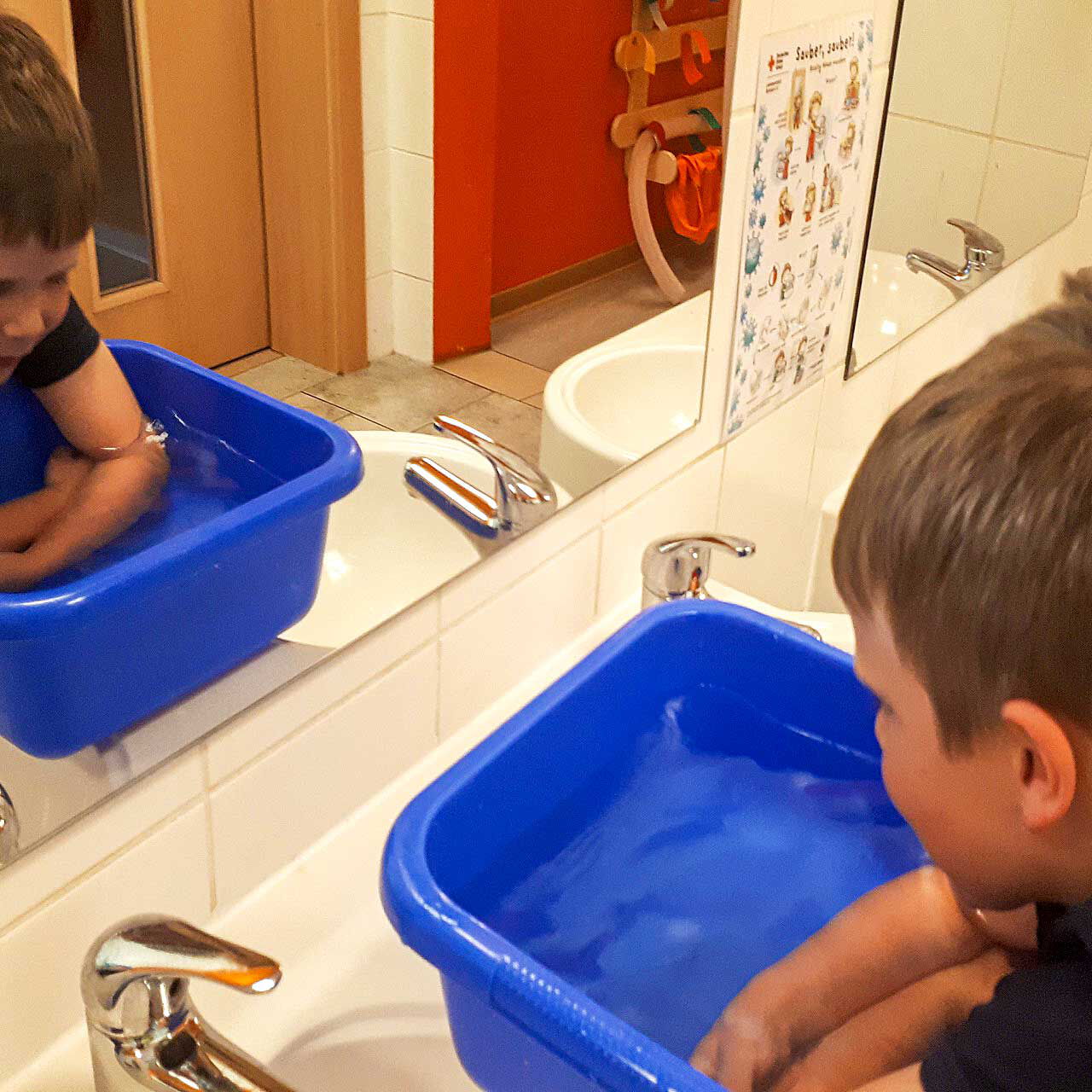 Ein Junge taucht seine Armen in eine blaue Schüssel mit Wasser.