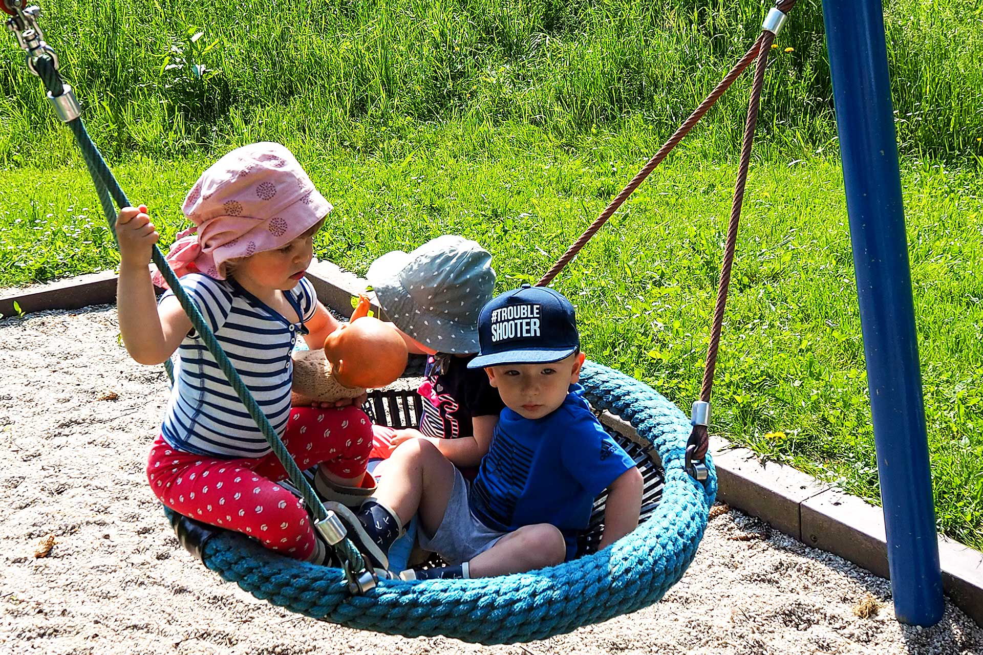 Drei Kinder sitzen in der Nestschaukel.