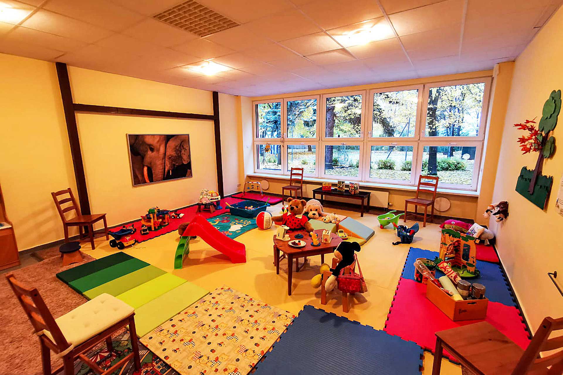 Ein große Spielezimmer mit Rutsche, Spielzeug, Sportmatten, Spielteppiche und Kindertische mit Stühle.