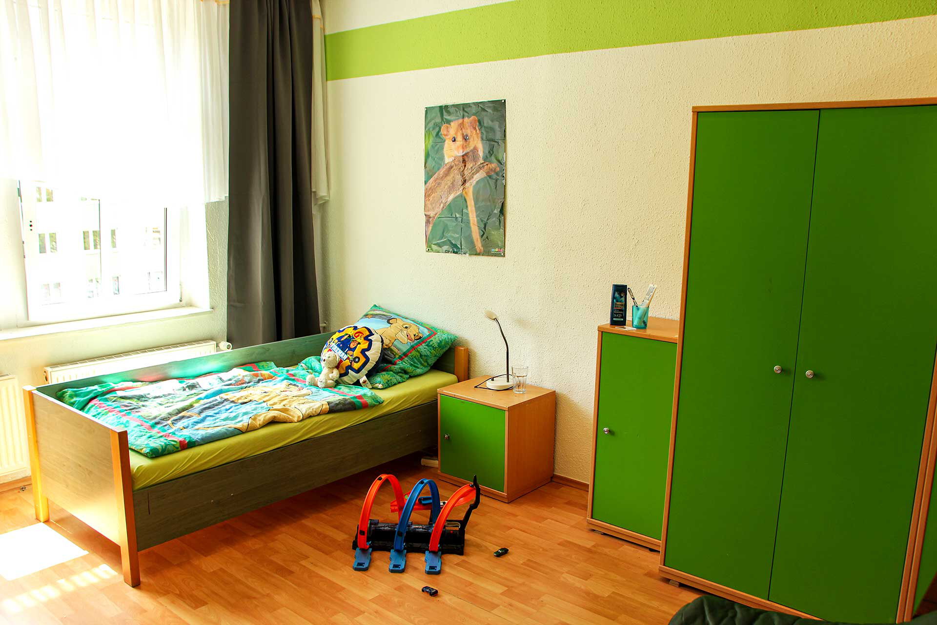 Ein Kinderzimmer mit einem Bett, Schrank und Nachttischschrank.