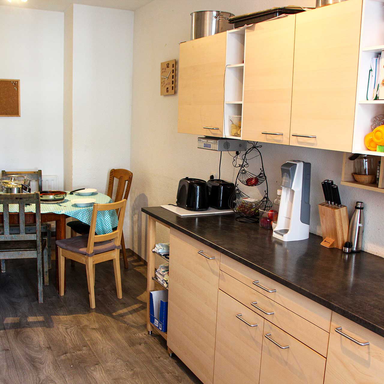 Eine Wohnküche mit Küchenzeile, Elektrogeräten und einem Rundtisch mit fünf Stühlen.