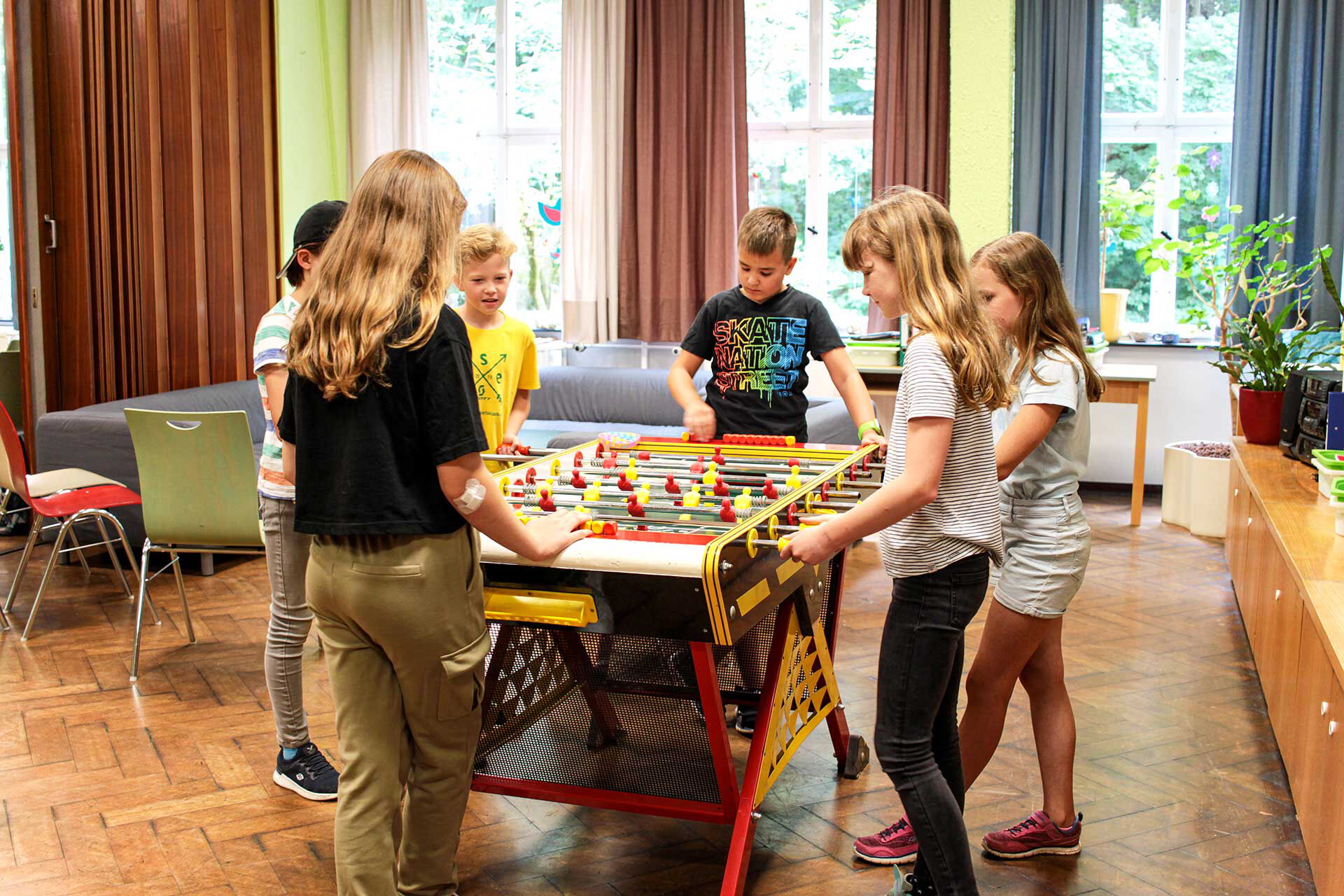 Im Veranstaltungssaal spielen sechs Kinder gemeinsam an einem Kickertisch.