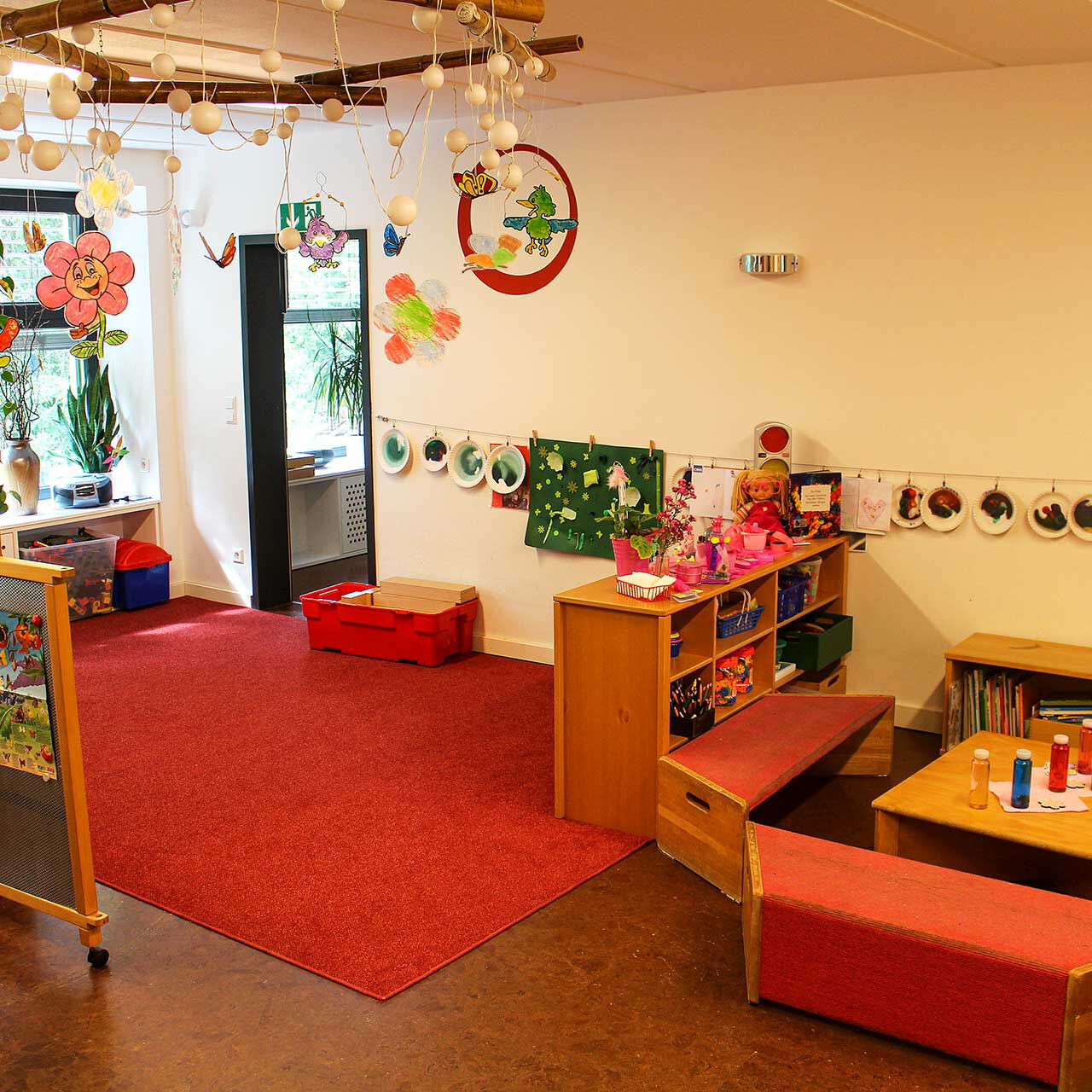 Die Spielecke im Gruppenzimmer beinhaltet einen Spielteppich mit verschiedenen Spielmöglichkeiten und einem Sitzbereich zum Malen und Basteln.