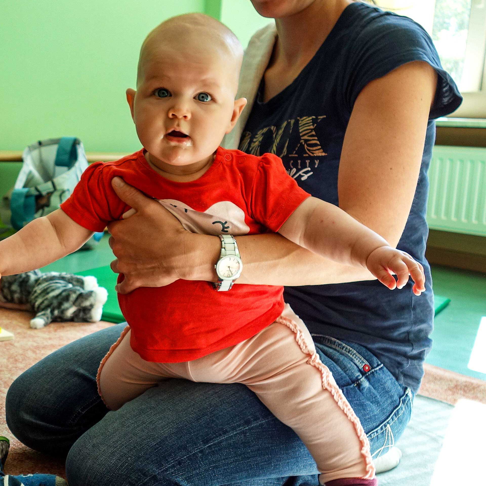 Ein Baby sitzt auf dem Schoß seiner Mutter und ist zum ersten Mal in der Krabbelgruppe.